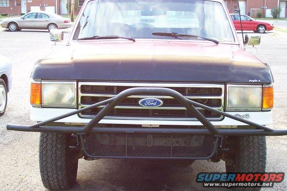1987 Ford Bronco front end with aftermarket brush guard and grille. Two other cars are visible in the background