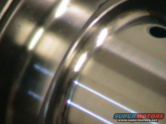 Close-up of a polished metal wheel rim with visible lug nut holes and reflective highlights