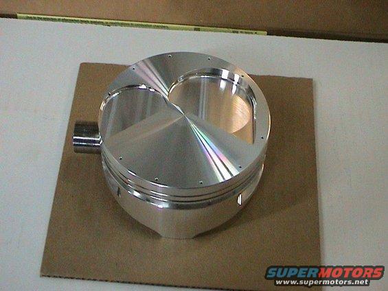 Polished aluminum piston with a domed top, resting on cardboard