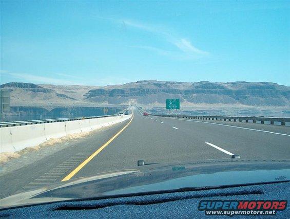 Highway overpass with mountains in the background and a green highway sign