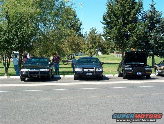 Three sedans parked on asphalt, one with hood open. The middle car has a push bar