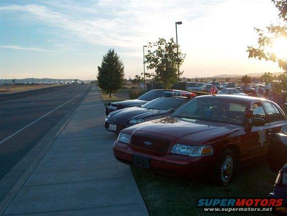 Red Ford Crown Victoria police car parked next to other cars, with a police light bar on top. Sun is setting