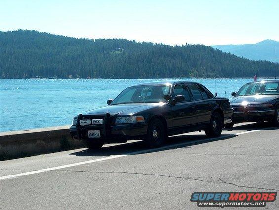 Black 2001 Ford Crown Victoria police car parked by a lake, another similar car behind it