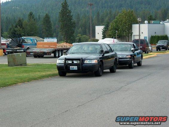 Front view of a black 2001 Ford Crown Victoria police car with a push bar. Another similar car is behind it
