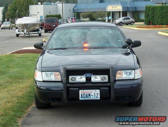 Front view of a black police car with a push bar and a light bar on top. License plate reads ADAM-12