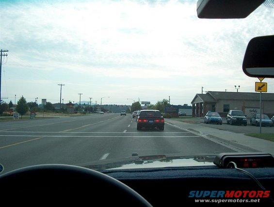 View from driver's seat looking at road ahead with other cars and buildings