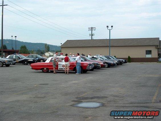 Several cars parked in a lot, including a red and white car labeled 'FIRE DEPT.' and some police cars
