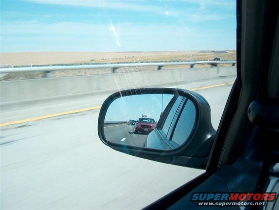 Red car seen in side mirror while driving on a highway