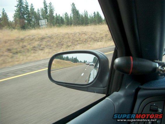 Interior view of a car on a highway, with other vehicles visible in the side mirror