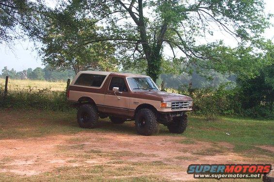 Brown and tan 1987 Ford Bronco with a body lift parked on a dirt patch