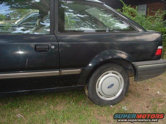 Side view of a dark sedan with a Ford logo on the hubcap. The body style suggests it's from the late 80s
