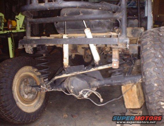 Off-road vehicle chassis with large tires, suspension components, and roll cage. Wood blocks support the frame