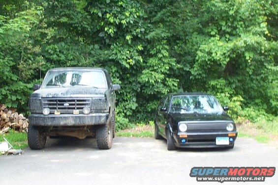 Front view of a black 1992 Ford Bronco parked next to a black Volkswagen Golf