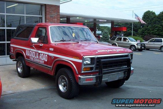 Red Ford Bronco fire truck with white stripes and "MAGNOLIA ROAD FIRE COMPANY" text, parked outside a building