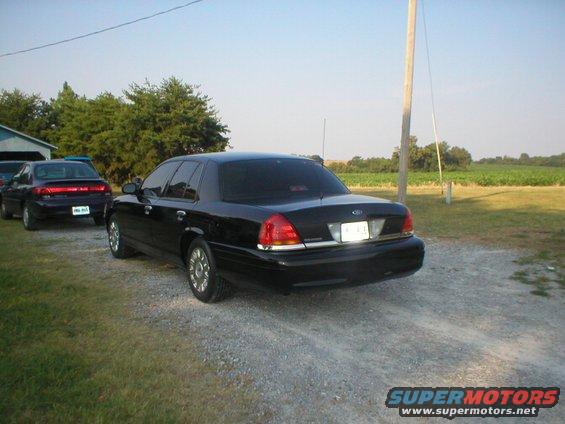Black sedan parked on gravel, rear view. License plate is visible
