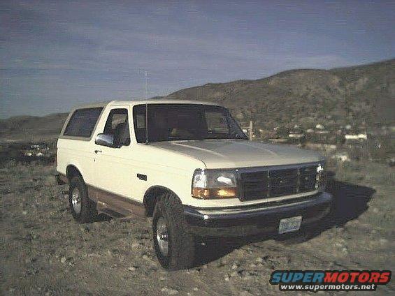 White 1992 Ford Bronco with wood paneling on the lower body, parked on a dirt lot with hills in the background