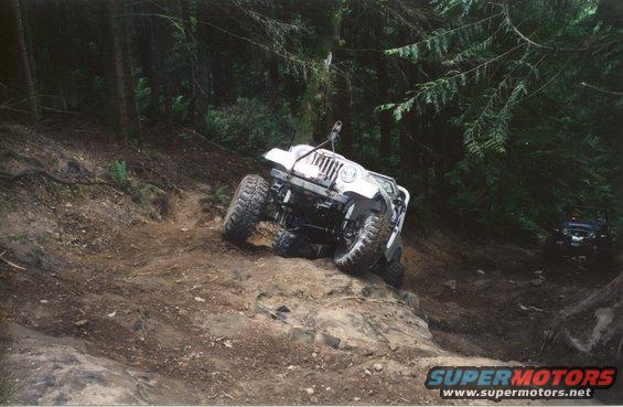 White Jeep Wrangler climbing a rocky, wooded trail