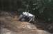 1990 Ford Bronco - A white Jeep Wrangler navigates a steep, off-road trail with another vehicle visible in the background.