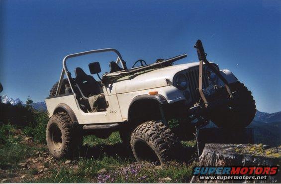 White Jeep CJ-7 with large tires on a dirt trail, front wheel on a stump