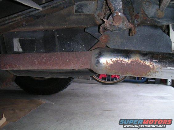 Underside view of a rusty exhaust pipe and vehicle frame with a spare tire visible