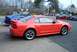 2004 Ford Mustang - Side view of an orange 2004 Ford Mustang, parked outdoors with a blue car nearby.