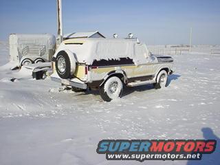 Snow-covered Ford Bronco parked next to a trailer in a snowy field