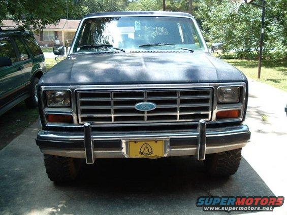 Dark blue Ford Bronco front view, dusty hood, chrome grille, yellow license plate