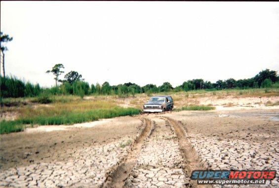 1985 Ford Bronco stuck in mud with tire tracks leading away