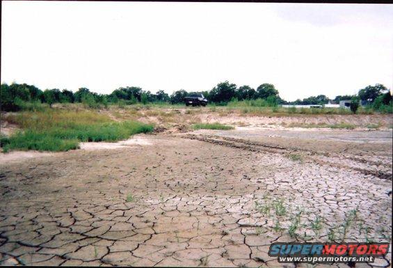 Truck in a dry, cracked earth landscape with trees in the background