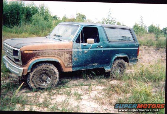Mud-covered Ford Bronco with mismatched front end, parked off-road