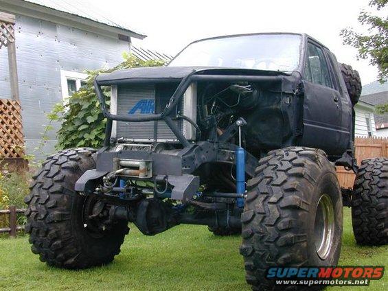 Black modified truck with oversized tires, exposed engine, and a winch