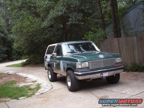 Green SUV, possibly a 1987 Ford Bronco, parked outside with bodywork visible on the fenders and doors