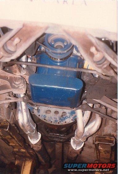 Underside view of an engine with blue valve covers and chrome exhaust headers
