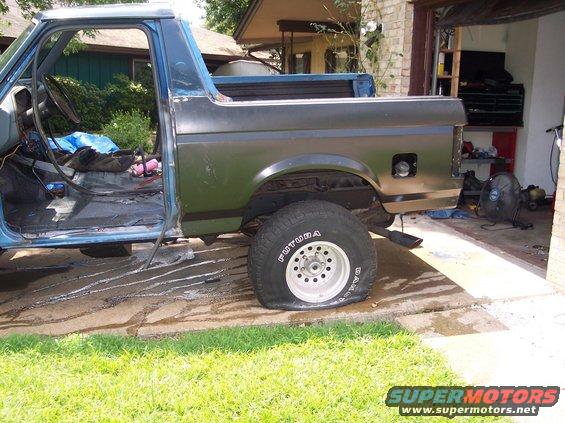 Side view of a blue and green SUV with a flat tire and missing door, parked in a driveway
