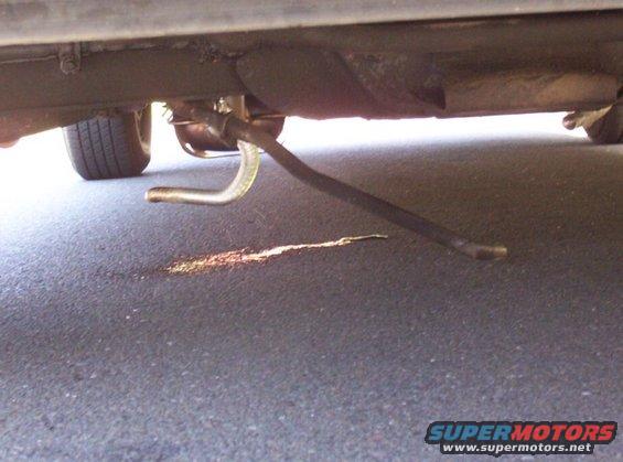 Undercarriage of a vehicle showing a bent metal pipe and a puddle of fluid on the ground