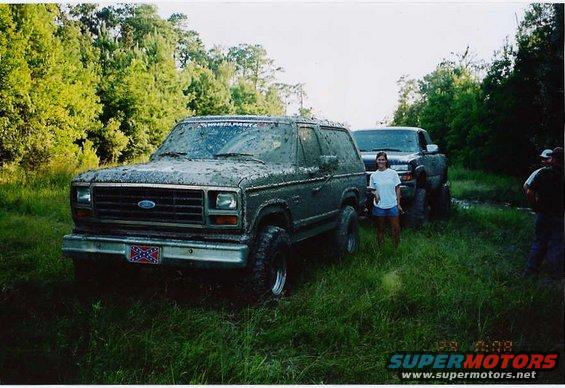 Mud-covered 1980 Ford Bronco parked next to a pickup truck in a grassy area