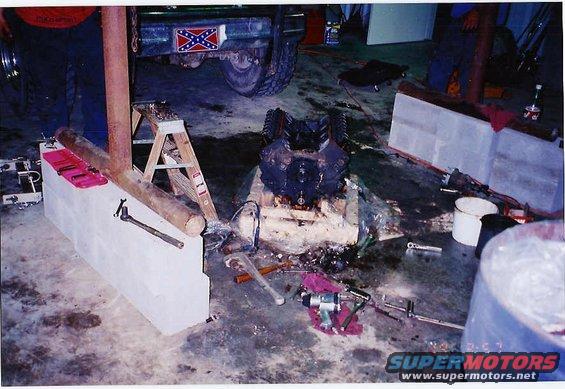 Engine block on floor, tools scattered around. Vehicle with Confederate flag sticker visible in background
