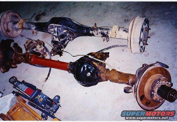 Two vehicle axles, one with a red driveshaft, and a jack