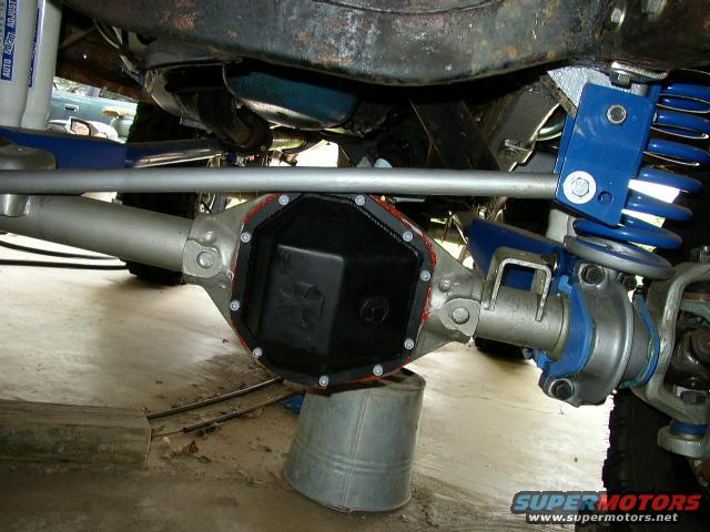 Close-up of a rear axle with a black differential cover that has a cross emblem. Blue suspension components are visible