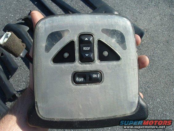 Hand holding a car's overhead console with buttons for 'ROOF', 'ON', and 'OFF'