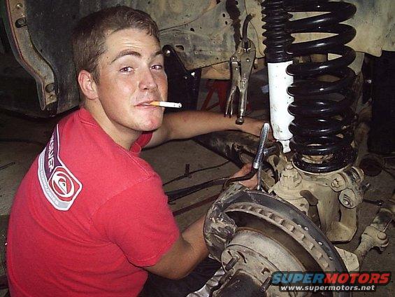 guy with cigarette in mouth working on front suspension of off-road vehicle