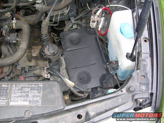 Engine bay with battery terminals, coolant reservoir, and black cover plate