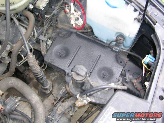 close-up of car engine bay with battery terminals, hoses, and fluid reservoir