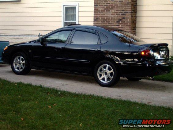 Black sedan parked on driveway, side view. Visible spoiler and aftermarket wheels