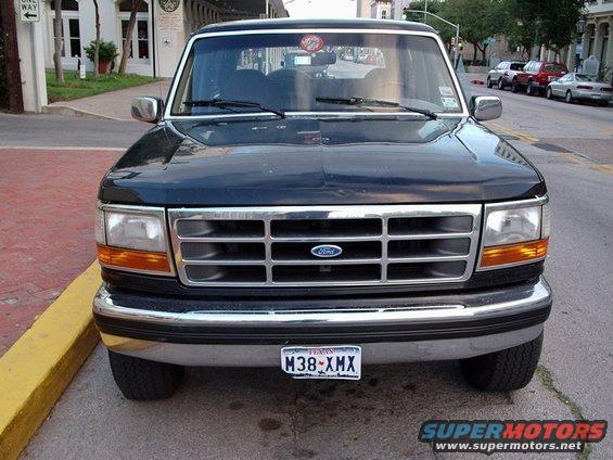 Front view of a dark-colored Ford Bronco parked on a street. It has a chrome grille with a Ford logo and a Texas license plate
