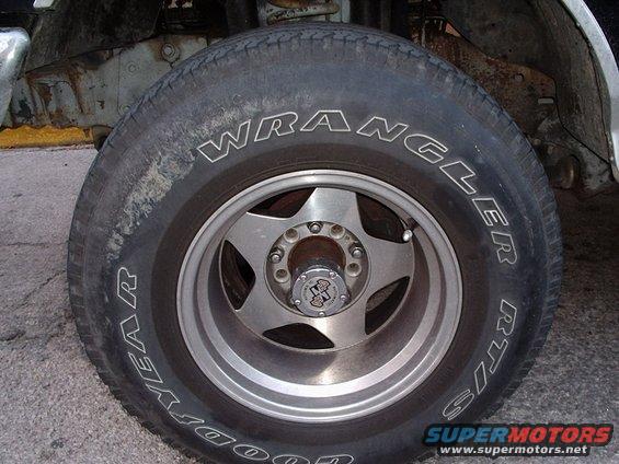 Close-up of a Goodyear Wrangler RT/S tire on a five-spoke alloy wheel, showing rust on the vehicle's frame