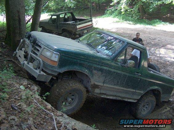 Green 1992 Ford Bronco navigating a steep dirt incline, another Bronco behind it