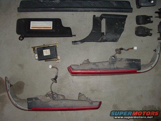 Car parts including a sun visor, control module, and taillight assemblies laid out on a concrete floor