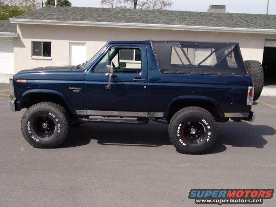 Dark blue 1984 Ford Bronco side view with soft top and spare tire on back