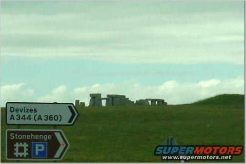 Stonehenge monument on a grassy hill with road signs pointing to Devizes and Stonehenge